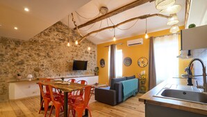 A cozy living area with a stone wall, wooden dining table, red chairs, and a grey sofa. - Unique charm - Clim - 6 pers in the heart of Carca (Carcassonne)