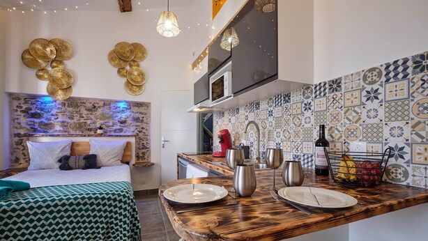 A compact bedroom with a bed, bedside table, and a headboard with wall art. Adjacent is a kitchen with a wooden countertop, a microwave, and a tiled backsplash. - Comfortable & bright studio - Air conditioning - Centre (Carcassonne)