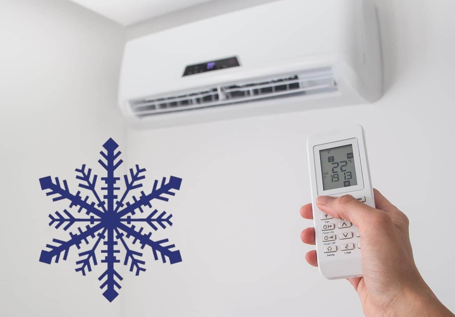 Une main tenant un thermostat doté d’un écran numérique, placé devant un appareil de climatisation fixé au mur.