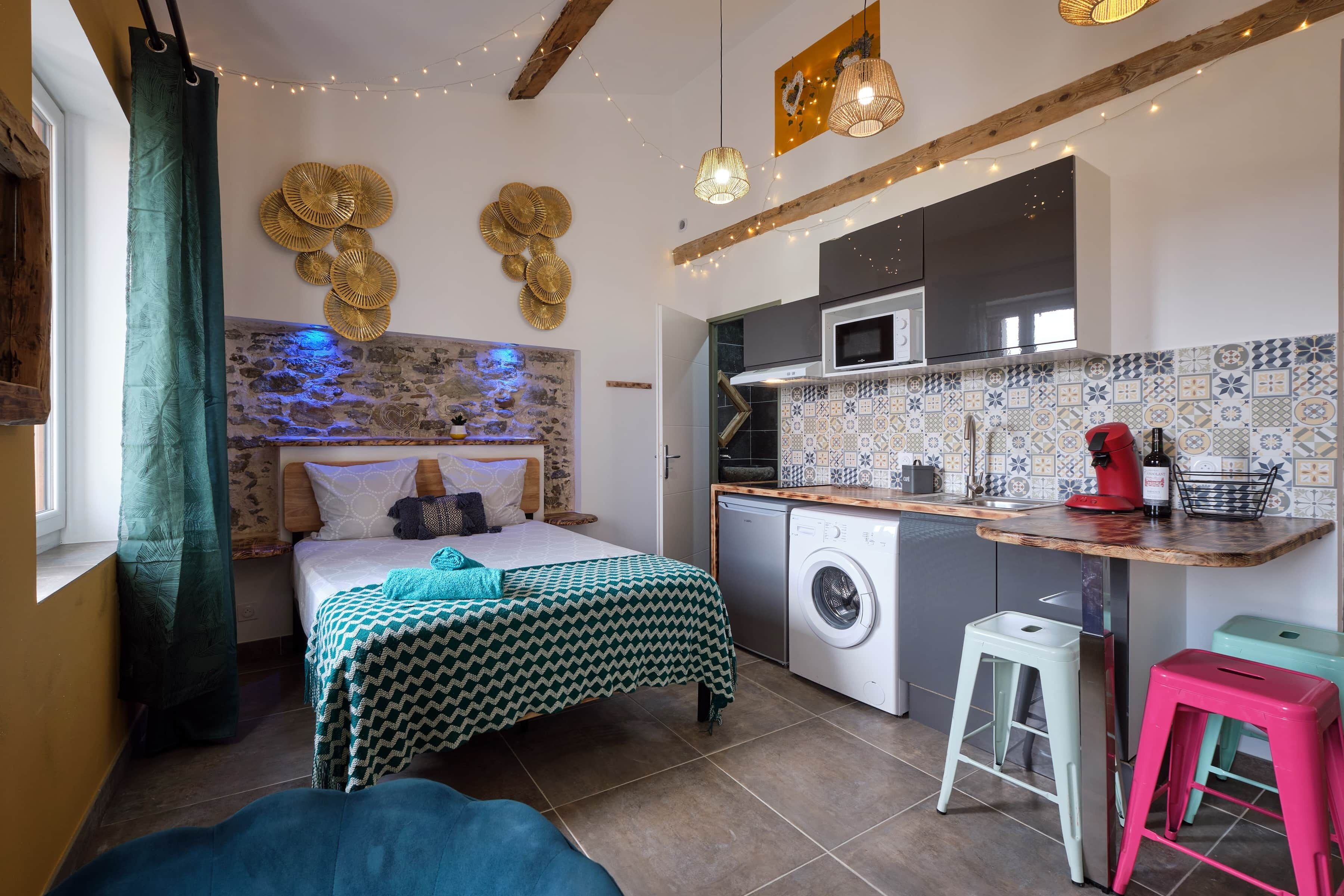 A compact bedroom with a bed, a washing machine, and a kitchenette.