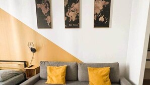 Ein modernes Wohnzimmer mit einem grauen Sofa, zwei gelben Kissen und drei Weltkarten an der Wand.
