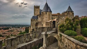 Eine historische Steinburg mit mehreren Türmen und einem befestigten Eingang, mit Blick auf eine Stadtlandschaft.