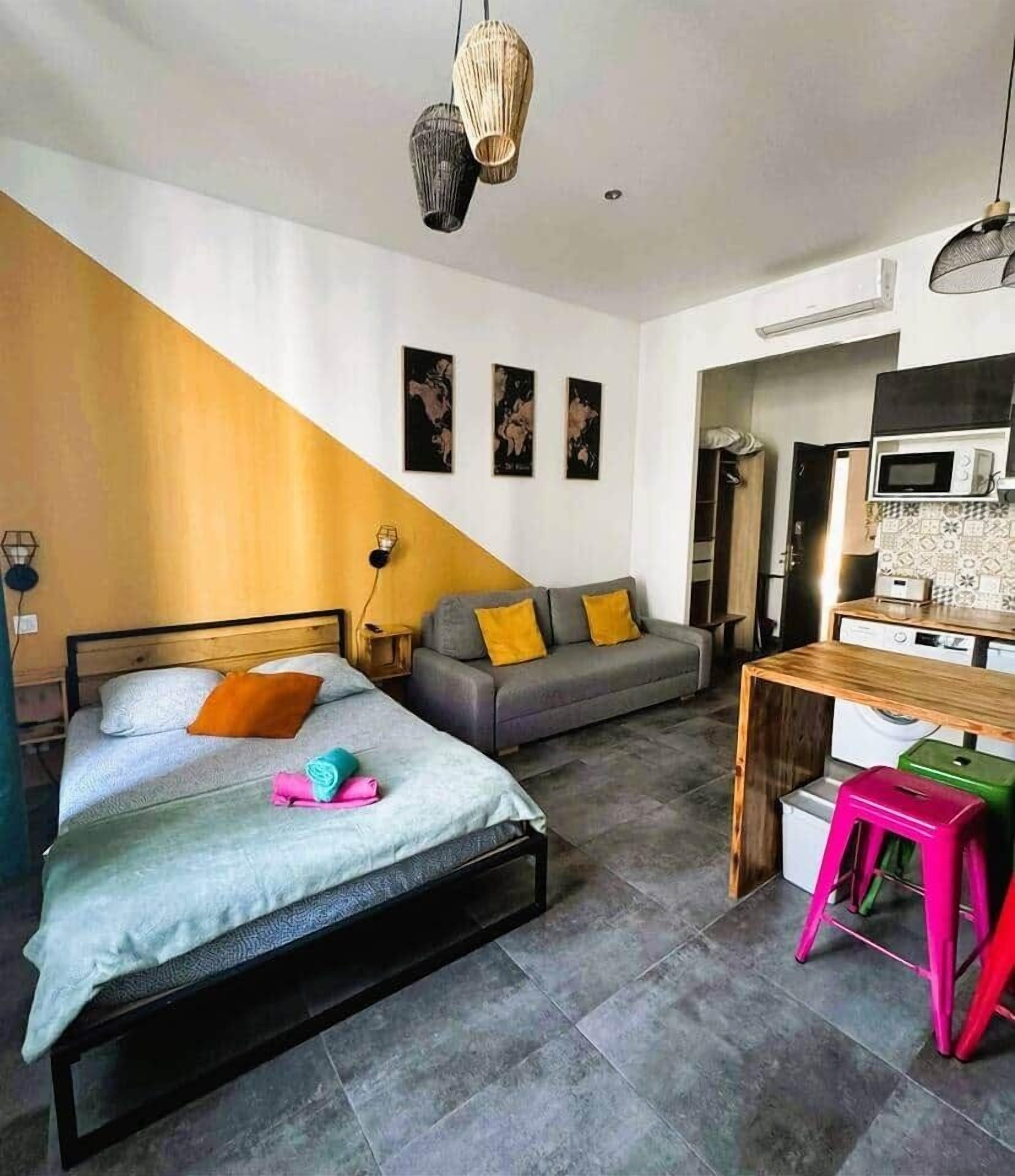 A modern bedroom with a bed, a sofa, a desk, and a kitchenette.
