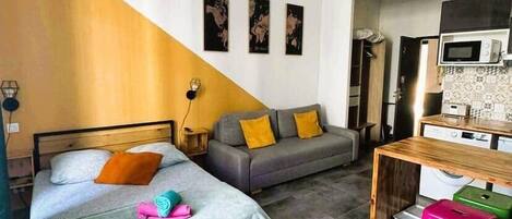 A modern bedroom with a bed, a sofa, a desk, and a kitchenette.