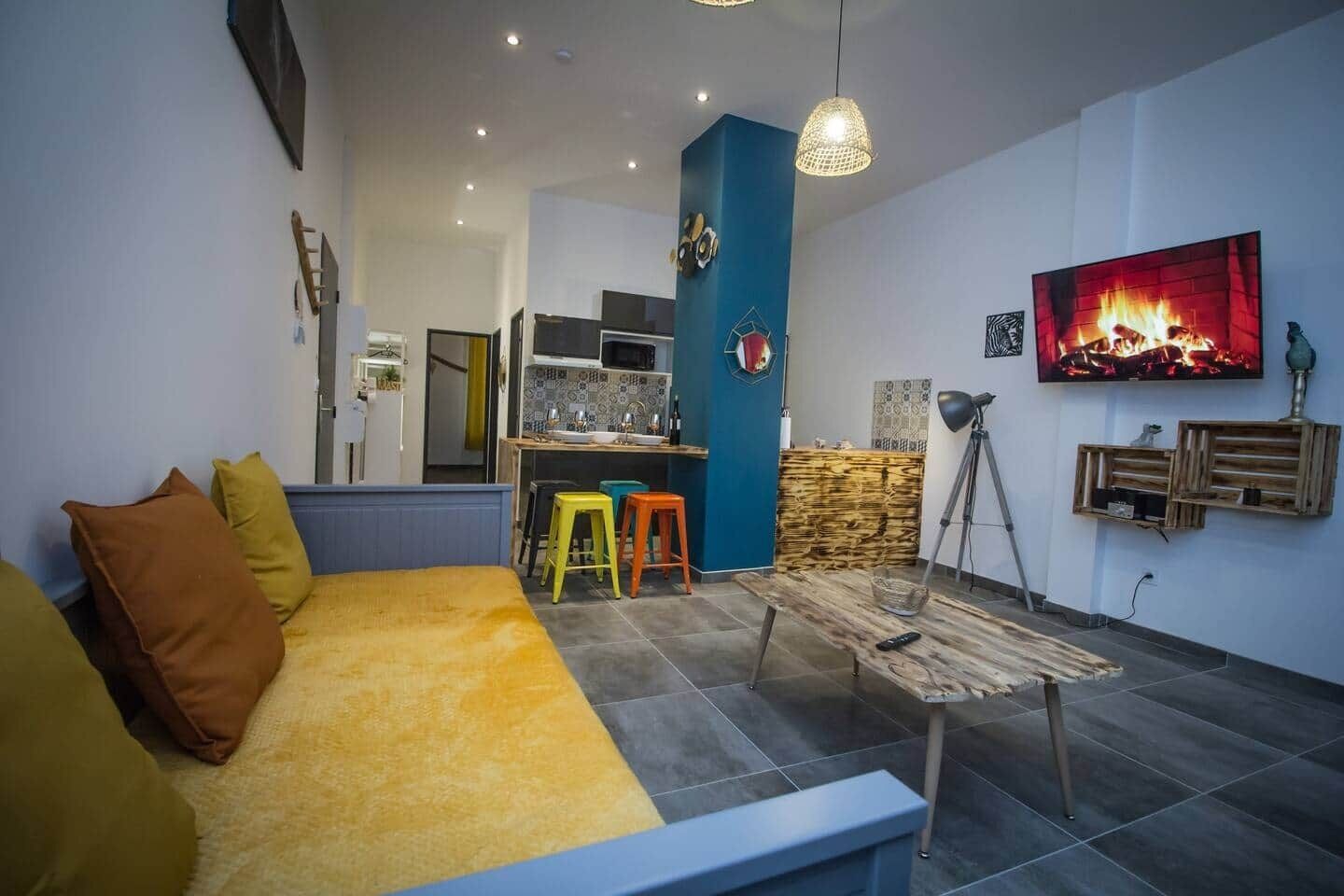 Un saló modern amb un sofà, tamborets de colors, una taula de centre i una cuina al fons.