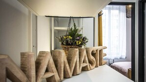 Una habitación con una mesa blanca mostrando letras de madera que deletrean “NAMASTE” y una cesta de mimbre con flores.