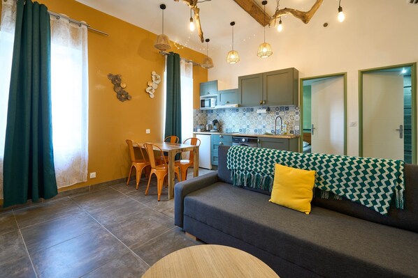 A compact living space with a sofa, dining table, chairs, and a kitchenette.