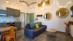 A modern kitchen with a tiled backsplash, a dining area with a wooden table and chairs, a sofa with a throw blanket, and a round coffee table. - Apartment 4 pers Calme & Confort - Clim - Centre (Carcassonne)