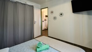 A hotel room with a bed, a bathroom visible through an open door, and a flat-screen TV mounted on the wall. - Apartment 4 pers Calme & Confort - Clim - Centre (Carcassonne)
