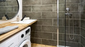 Ett modernt badrum med ett handfat i trä, en tvättmaskin, en dusch med ett justerbart duschmunstycke och en stor spegel.