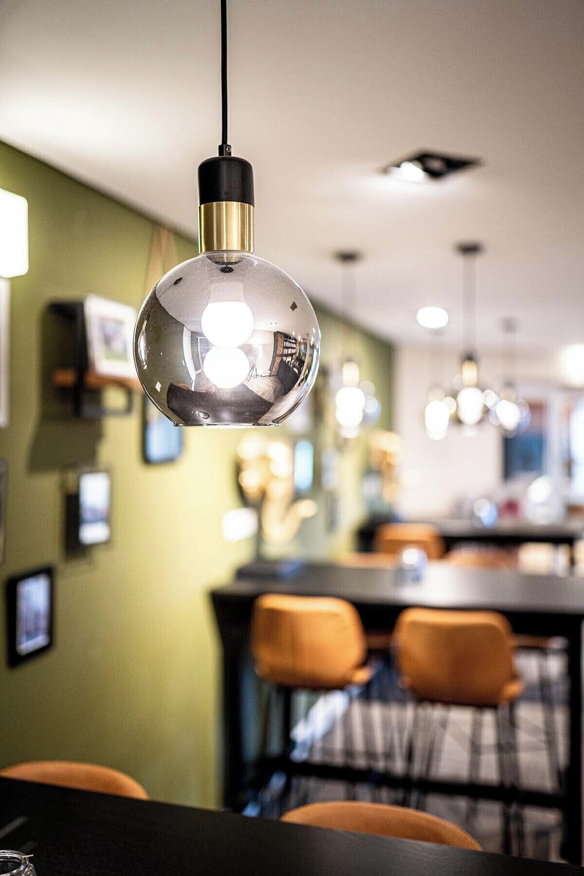 A modern dining area with a round pendant light, green walls, and orange chairs.