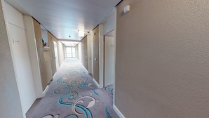 Pasillo de hotel con alfombra estampada, paredes blancas y puertas con números de habitación.