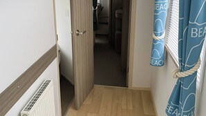 Een hal met een houten vloer, een radiator, een deur naar een badkamer en blauwe gordijnen met een strandthema.