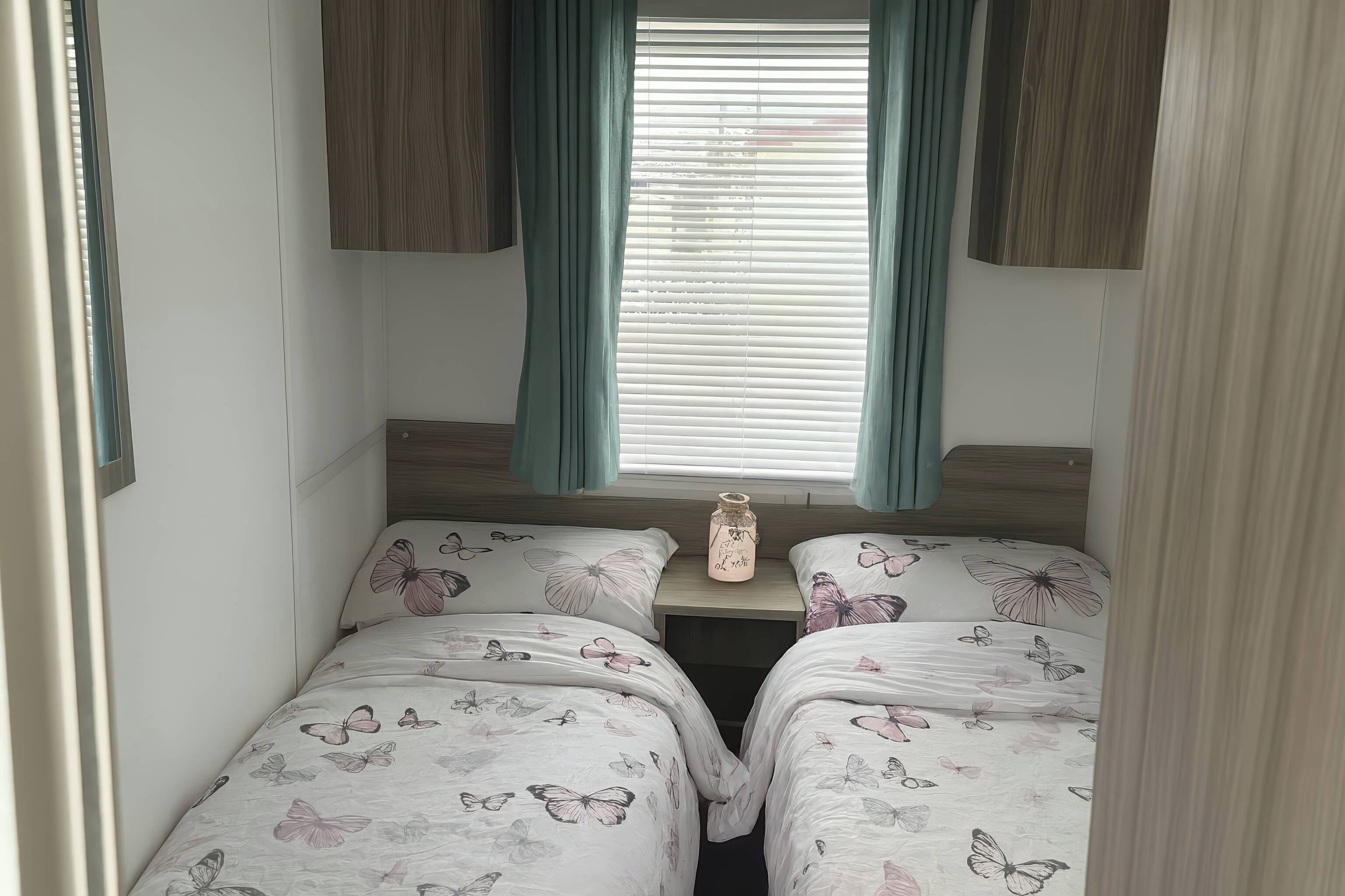 A bedroom with two single beds, a nightstand, and a window with blinds.
