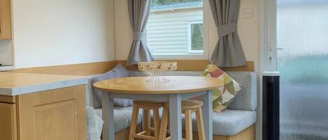 A compact kitchenette with a wooden countertop, a small round table, and a bench with cushions.