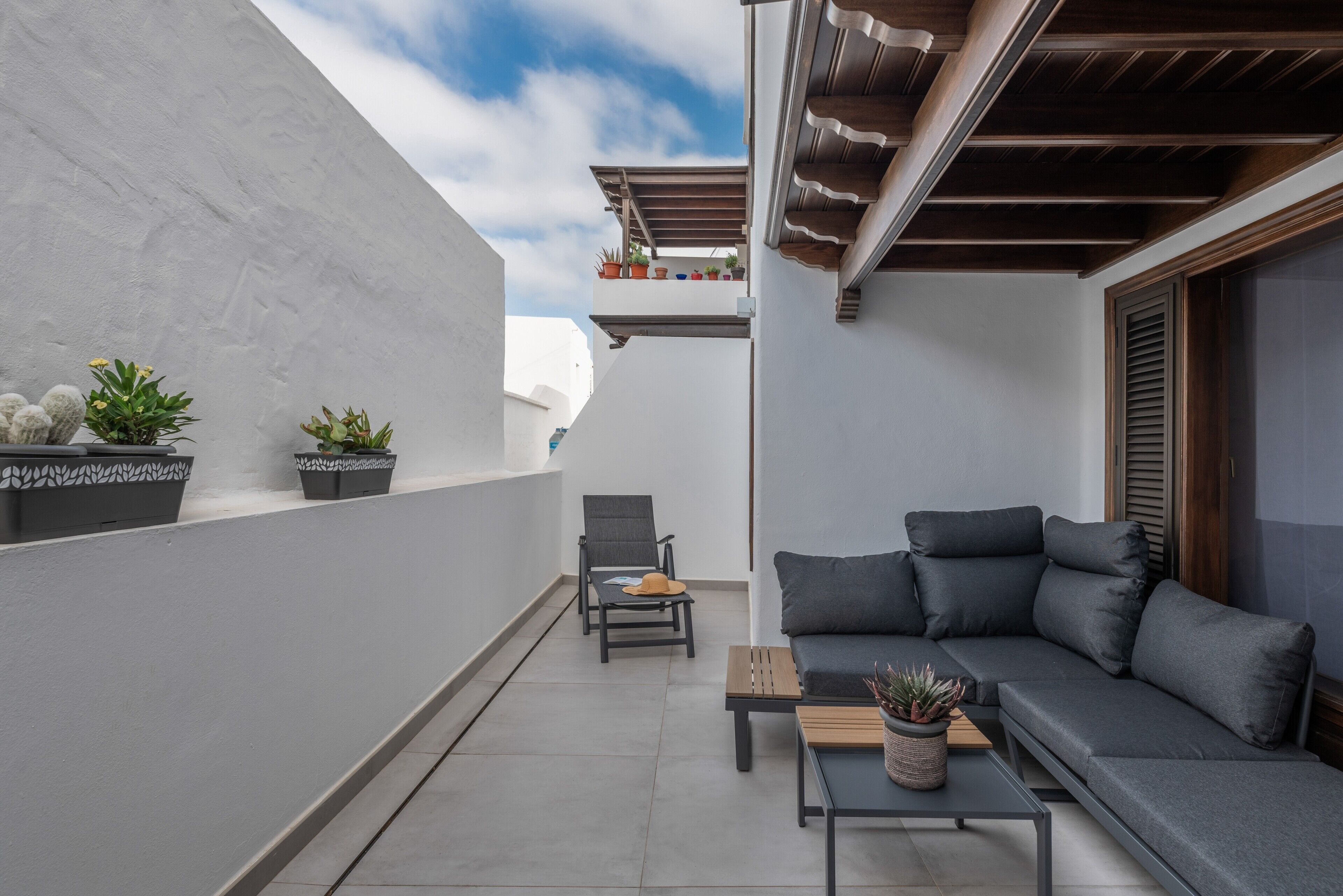 Un balcone con un divano grigio, una sedia, un tavolino e piante in vaso.