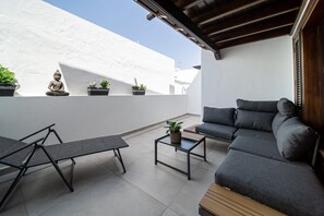 A modern outdoor seating area with a sofa, chairs, and a small table, surrounded by potted plants and a Buddha statue.