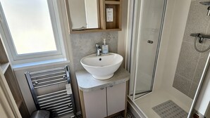A modern bathroom with a white sink, a glass shower enclosure, and patterned floor tiles. - Ocean Edge Leisure Park - 21286 (Morecambe)