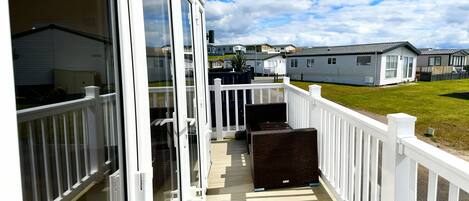 A covered outdoor area with a wooden deck, white railings, and a view of mobile homes in the background.