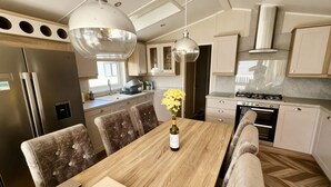 A modern kitchen with a wooden dining table, four cushioned chairs, a wine bottle, and a vase of yellow flowers. - Ocean Edge Leisure Park - 21286 (Morecambe)