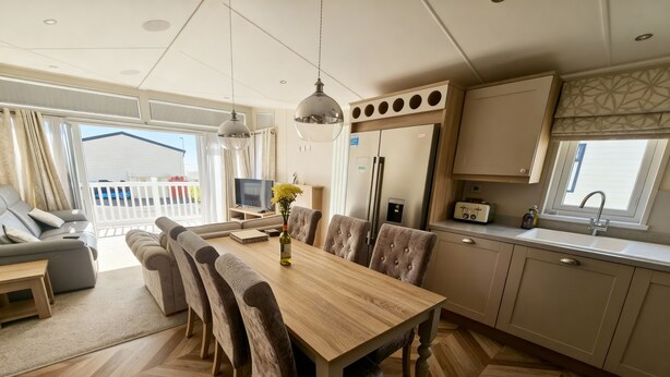 A modern kitchen with a wooden dining table, chairs, and a built-in refrigerator. - Ocean Edge Leisure Park - 21286 (Morecambe)