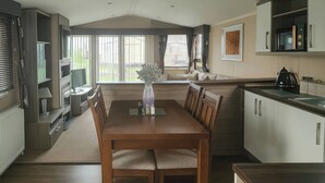 A modern kitchen with a dining area, large windows, and a view of the outdoors. - Whitehouse Leisure Park - 19057 (Abergele)