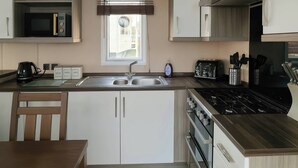A compact kitchen with a microwave, stove, sink, and wooden cabinets. - Whitehouse Leisure Park - 19057 (Abergele)