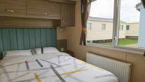 A bedroom with a bed, a window, a radiator, and a view of neighboring houses. - Whitehouse Leisure Park - 19057 (Abergele)