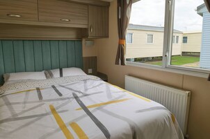 Quarto com cama, janela, radiador e vista para casas vizinhas.
