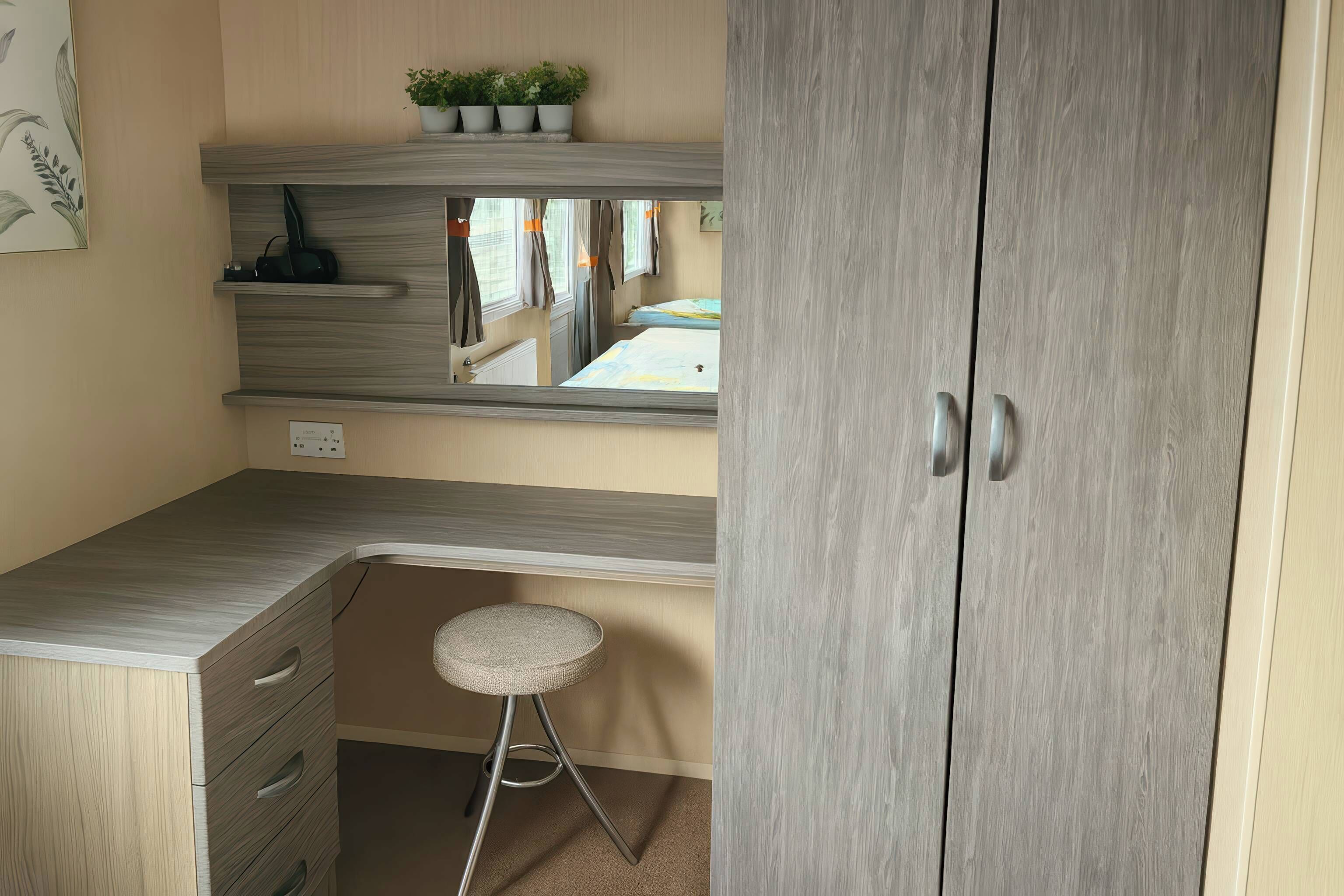 Une pièce avec une armoire grise, un petit tabouret, une étagère avec des plantes et un miroir qui reflète la pièce.