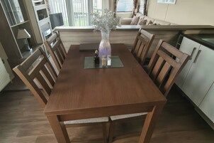 Un coin repas avec une table en bois, des chaises, un vase de fleurs et une fenêtre avec des stores.