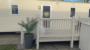 A mobile home with a fenced deck, a potted plant, and a chimney.