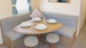 A dining area with a round table set for four, a grey cushioned bench, and two round stools.