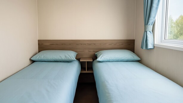 A twin room with two single beds, a wooden headboard, a small table, and a window with curtains.