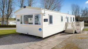 A mobile home with a covered porch, a small attached garage, and a clear sky in the background.