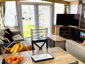 Ein modernes Wohnzimmer mit einer Couch, einem Couchtisch mit einem Laptop und Obst, einem Fernseher und einem Kamin.