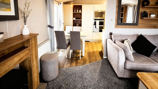 A modern living room with a grey sofa, a wooden coffee table, and a dining area with a white table and chairs. - Thornwick Bay Holiday Village - 20633 (Bridlington)