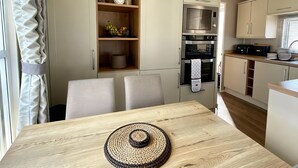 A compact kitchen with a microwave, oven, and a small sink. There are two chairs and a table with a woven placemat. - Thornwick Bay Holiday Village - 20633 (Bridlington)