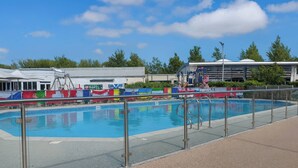 Ein Schwimmbecken mit Metallgeländer, ein überdachter Bereich mit bunten Markisen und ein Gebäude im Hintergrund.
