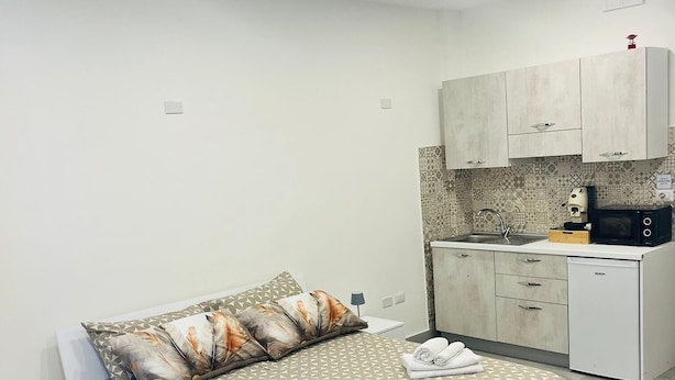Une chambre à coucher comprenant un lit, des oreillers, une table de chevet et une petite kitchenette équipée d’un four à micro-ondes, d’un évier et de placards.