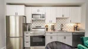 A modern kitchen with white cabinets, stainless steel appliances, and a green chair.