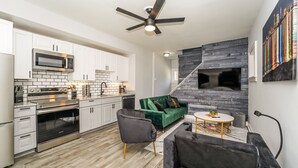 A modern kitchen with white cabinets, stainless steel appliances, and a green sofa in a living area with a fireplace.