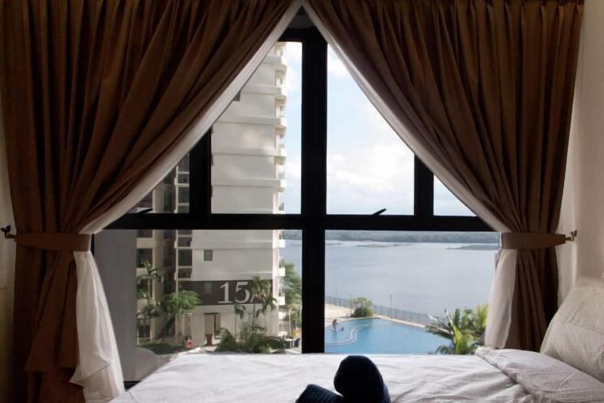 Une chambre d’hôtel avec une grande fenêtre, un lit et une vue sur un immeuble et une piscine.