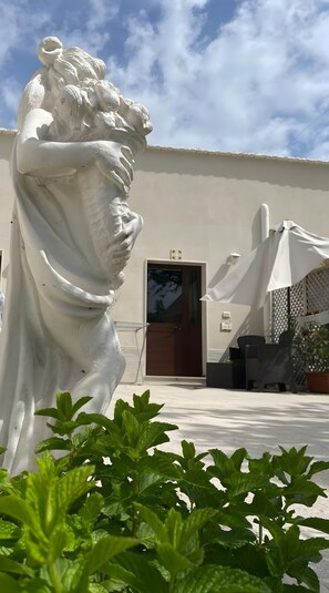 A white statue in front of a building with a door and outdoor seating.
