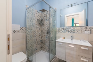 Une salle de bain équipée d’une douche, de toilettes et d’un lavabo, avec des carreaux décoratifs et un miroir.