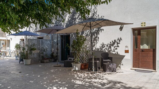Ein Außenbereich mit Terrasse, üppigen Pflanzgefäßen, Gartenmöbeln und Sonnenschirmen, die Schatten spenden.