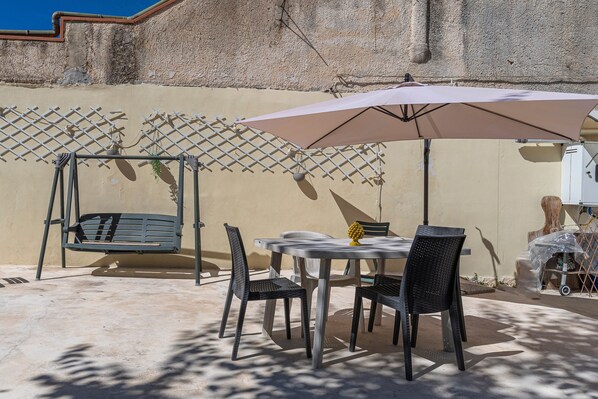 Un patio con una mesa, sillas, una hamaca y una sombrilla.