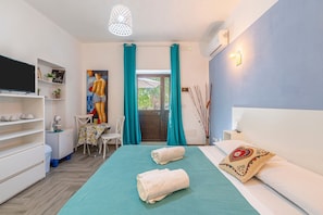 Une chambre d’hôtel comprenant un lit, une télévision, un bureau avec une chaise et une vue sur l’extérieur par une porte.