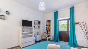 Ein Schlafzimmer mit Bett, Fernseher, Schreibtisch, Stuhl und einem Fenster mit Vorhängen.