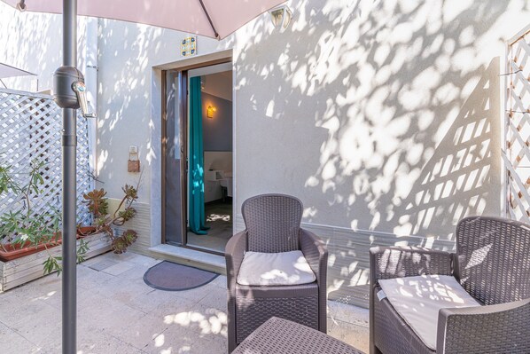 Un espace extérieur aménagé avec des meubles en osier, une porte donnant sur une pièce et une clôture blanche en treillis.